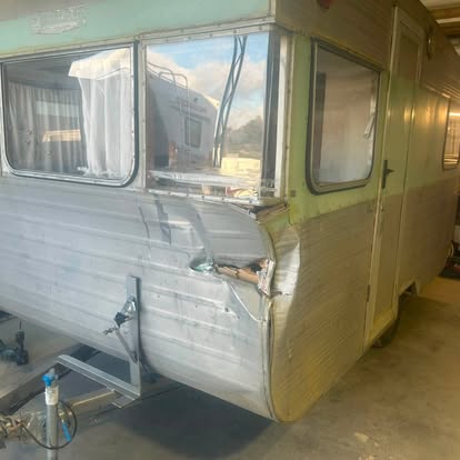 The same caravan mid restoration with one side stripped back to bare aluminium beside the original faded green paint