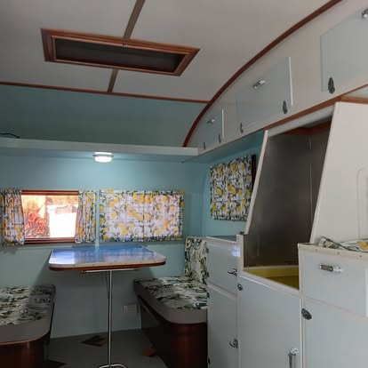 Restored caravan interior with pale blue walls, lemon print curtains and a timber edged dinette table