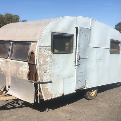 A vintage caravan before restoration, with heavy rust, peeling paint and a damaged rear panel